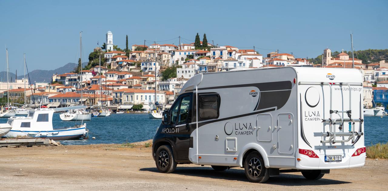 White motorhome parked by the sea, with an island town and sailing boats in the background